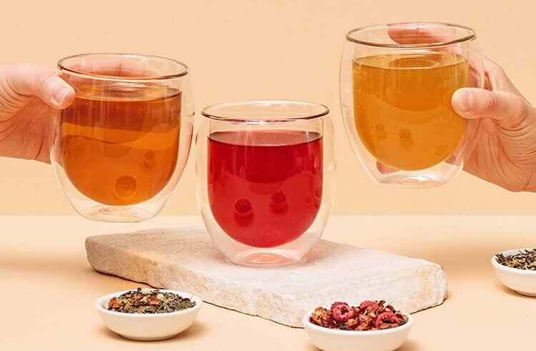 article2a-muesli.jpg Drei transparente doppelwandige Teeglaeser mit verschiedenen Tees gefuellt neben Blatttees in kleinen Schaelchen